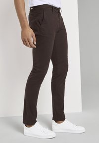 Pantaloni slim-fit marroni in cotone, con tasche frontali e una trama liscia, abbinati a sneakers bianche.