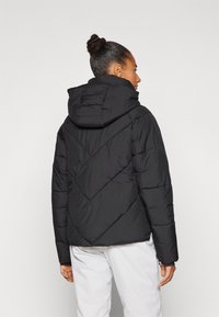 Veste en duvet noire avec capuche, dotée d'un design matelassé et de coutures diagonales. Le tissu a une texture lisse et est isolé pour offrir de la chaleur.