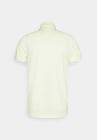 Polokošile v měkké žluté bavlně, krátké rukávy, klasický límec a rovný střih bez viditelných označení či dekorací.