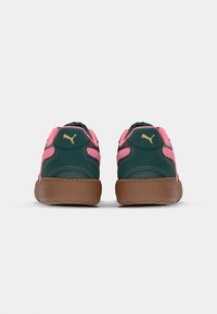 Green suede athletic shoes with pink accents, featuring a gum sole and gold logo detail on the heel. Rounded shape, padded collar.