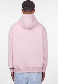 Lichtroze hoodie met een kangoeroezak, ribgebreide mouwen en onderrand. Beschikt over een grote capuchon en zacht katoen. Weergegeven vanuit de achterkant.