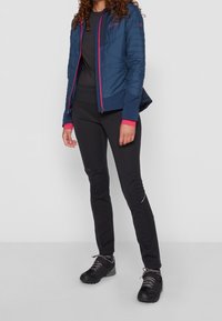 Marinblått vadderat jacka med rosa detaljer, parat med svarta tajta byxor och mörka skor. Klädseln har en sportig design och en strömlinjeformad form.