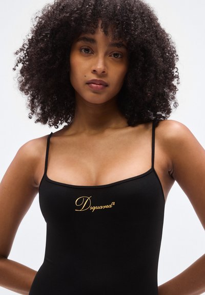 Haut noir ajusté à fines bretelles, en tissu texturé avec un logo doré brodé sur le devant, surface lisse et design minimaliste.