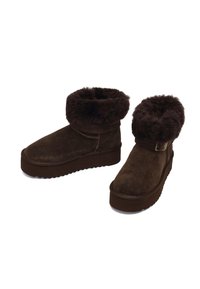 Braune Wildlederstiefel mit einem dicken, strukturierten, künstlichen Fellbund, flacher Gummisohle und verstellbarem Riemen. Lässiges Design, geeignet für kaltes Wetter.