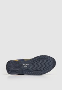 Las zapatillas Pepe Jeans cuentan con una suela de goma con un agarre texturizado, una parte superior de textil en combinación de azul marino y oliva, y detalles en color amarillo.