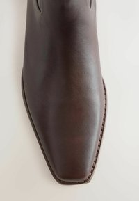 Close-up of a dark brown leather dress shoe with a squared toe and visible stitching along the edge.