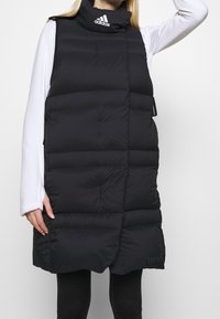 Sort puffervest med høj krave, quiltet tekstur og løs pasform. Har et broderet logo og sidelommer for funktionalitet.