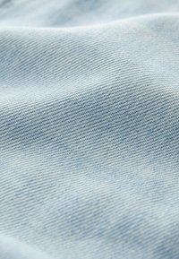 Tissu en denim bleu clair avec une texture lisse, présentant un subtil motif en sergé. La vue en gros plan montre de fins détails de couture.