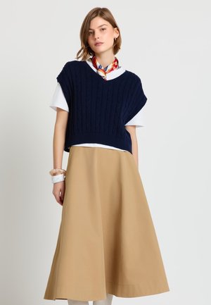 Veston tricoté bleu marine à col en V avec un motif torsadé porté sur une chemise blanche, associé à une jupe fluide beige. Tissu lisse et coupe décontractée.