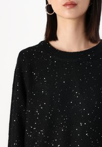 Svart tröja med rund halsringning, texturerad stickning och spridda silverpaljetter för extra glans.