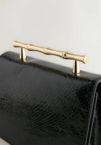 Černá kabelka s texturovaným materiálem inspirovaným plazy. Má zlaté rukojeti ve stylu bambusu a elegantní tvar. Elegantní a moderní design.