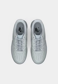 Svijetlosivi Nike Air tenisice s glatkom kožom, perforiranim vrhom, usklađenim vezicama i suptilnim logotipom na ulošcima.
