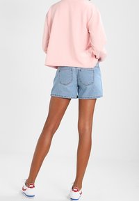 Ljusrosa croppad sweatshirt, blå denimshorts med bakfickor och vita sneakers med röda accenter. Slät tyg och avslappnad passform.