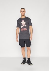 Mørkegrå bomull T-skjorte med grafisk trykk og teksten "BREAK MORE THAN A SWEAT." Kombinert med svarte shorts og sportssko.