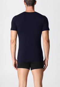 T-shirt a maniche corte blu navy realizzato in tessuto morbido, design aderente, collo tondo, con una parte posteriore liscia, indossato con pantaloni corti neri.