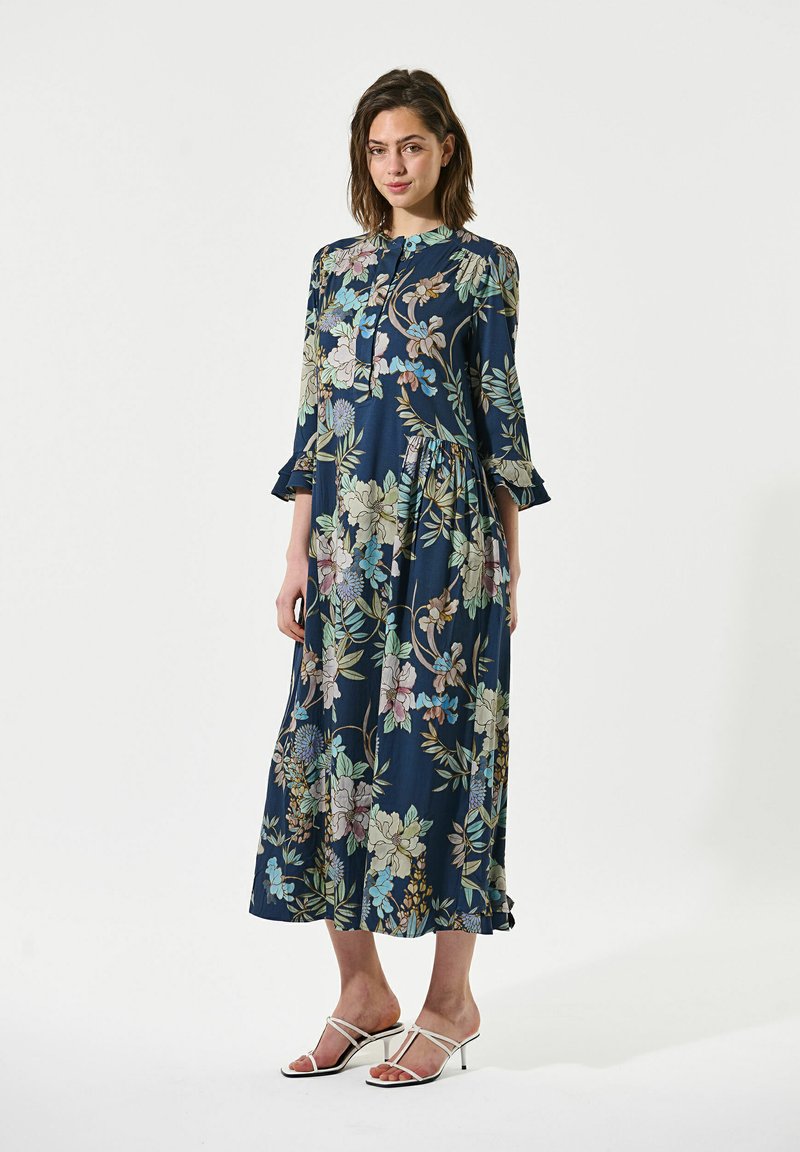 Marineblaues Kleid mit floralem Muster, hochgeschlossenem Kragen, dreiviertel Ärmeln, gestuftem Rock und leichtem Stoff. Mit Rüschen verziert.