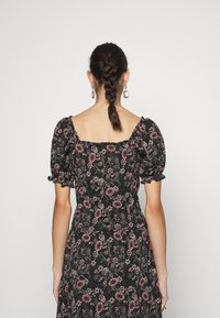 Vestido preto floral com mangas curtas bufantes, decote quadrado e corpete justo. Decorado com flores cor-de-rosa e brancas sobre um fundo escuro.