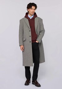 Šedý vlněný kabát s přizpůsobeným střihem, jednorušný design, klopy s výstřihem, doplněný vínovou kapucí a tmavými kalhotami. Hnědé boty.