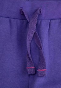 Fioletowe bawełniane spodnie z teksturowanym pasem i sznurkiem do ściągania z kontrastującym czerwonym przeszyciem. Gładki materiał o miękkim wykończeniu.