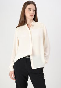 Cream button-up blouse with textured yoke, long sleeves, and a relaxed fit. Soft, lightweight fabric with a smooth finish.