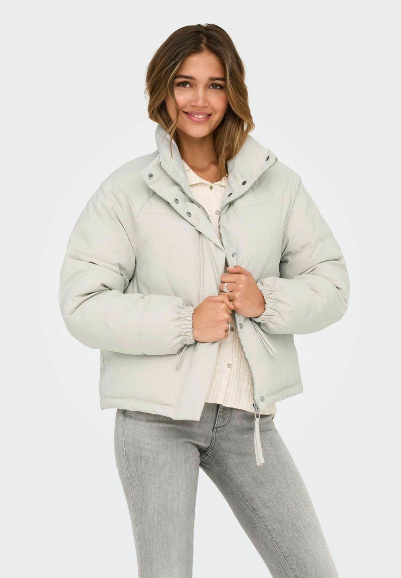 Helehall punnitud jakk kõrge kraega, elastsete mansettide ja trukkidega. Valmistatud siledast materjalist, kombineeritud valge särgiga.