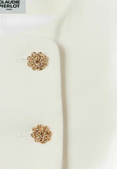 Blazer blanc en tissu texturé, avec deux boutons dorés en forme de rose comme accents à l'avant. Design simple et élégant.