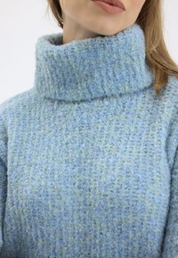 Svetlo modrý pletený rolák s textúrou a hrubým rebrovaným vzorom so subtílnymi zelenými akcentmi. Mäkkučký, teplý materiál.