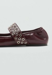 Ballet flat maroon yang terbuat dari kulit dengan tali lebar dan lubang perak, tekstur halus, dan desain ujung bulat.