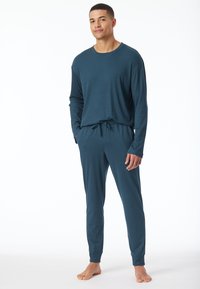 Ropa de estar para hombre en un color teal oscuro, hecha de una tela suave. Camiseta de manga larga con cuello redondo, combinada con pantalones con cordón y puños acanalados en los tobillos.