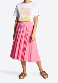 Hvid t-shirt med en pastelfarvet grafik, kombineret med et knælængde plisseret lyserødt skørt og brune mønstrede slip-in sandaler.