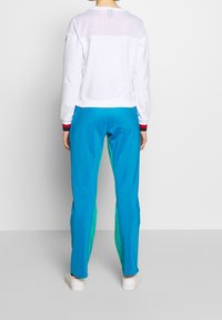 Biała bluza z siateczkową górną częścią, w połączeniu z niebieskimi spodniami z zielonymi bocznymi panelami. Ściągacze na rękawach i gładkie białe buty.