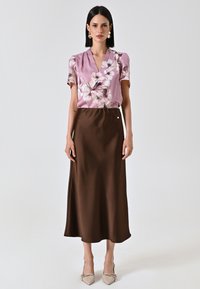 Korte mouwen roze blouse met bloemenprint; gecombineerd met een bruine satijnen midi-rok; model draagt beige puntige hakken; minimalistische accessoires.