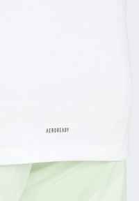 White athletic shirt featuring "AEROREADY" logo in black at the hem. Smooth fabric with a classic fit, suitable for active wear.