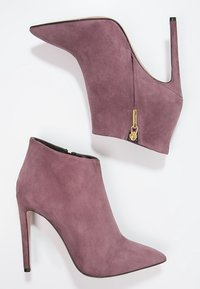 Fioletowe zamszowe botki za kostkę z wydłużonym noskiem i wysokimi obcasami w szpilkach. Posiadają boczny zamek błyskawiczny z ozdobnym złotym elementem.