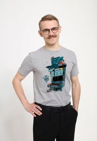 Camiseta gris de manga corta con un diseño gráfico colorido de un edificio con acentos de graffiti. Combina con pantalones negros.