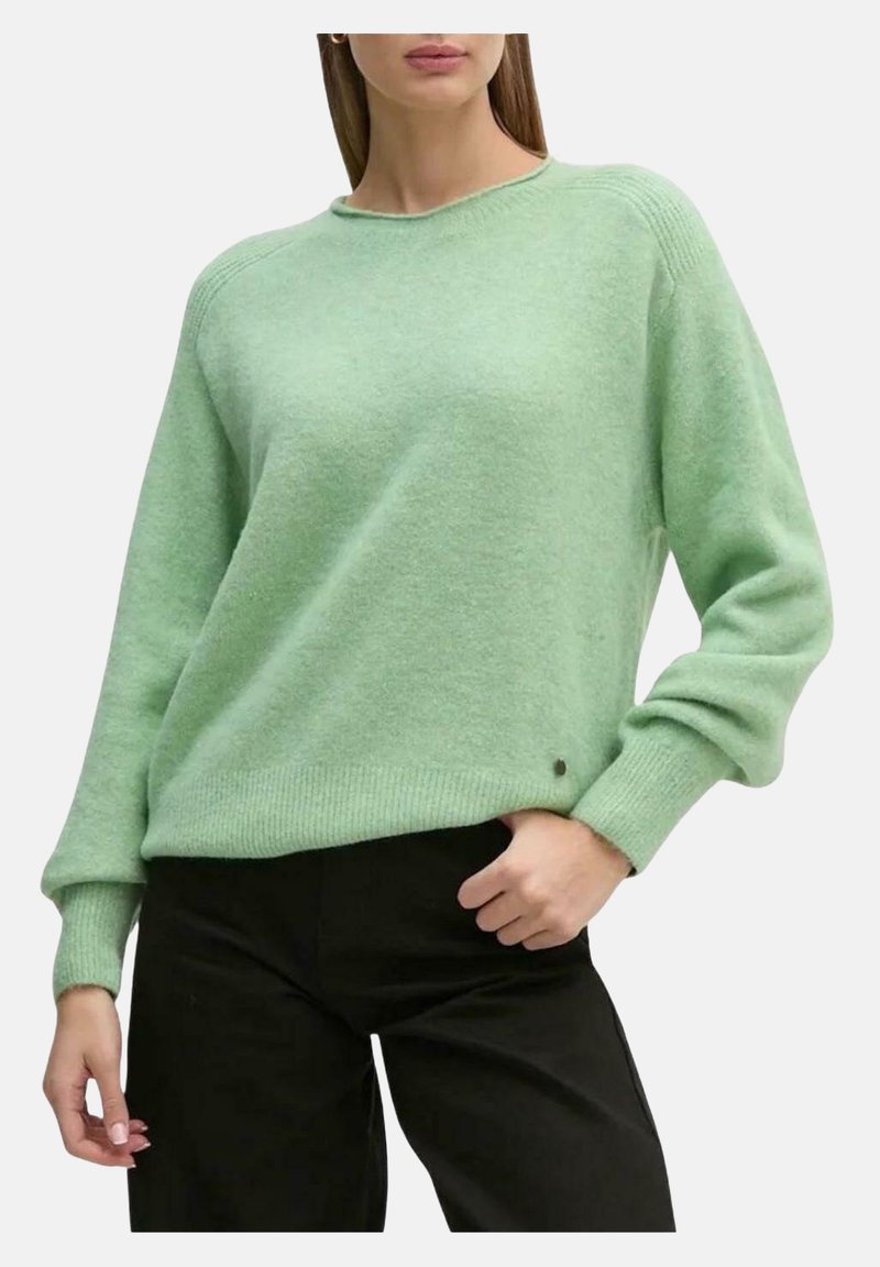 Maglione a maglia testurizzata di colore verde chiaro, con scollo a girocollo e polsini a coste. Presenta un piccolo logo decorativo all'orlo. Abbinato a pantaloni scuri.