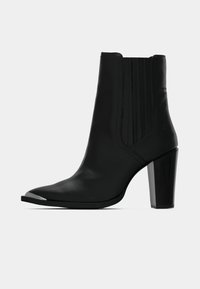 Melna ādas potīšu zābaku ar norādītu pirkstu, elastīgām sānu pannēm un augstu bloku papēdi; uz pirksta ir metāla akcenti.