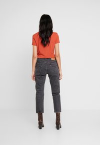 Orange kortärmad t-shirt i kombination med högmidjade svarta jeans med en klassisk femficksdesign och en läderpatch bak.