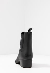Bottines noires en matériau lisse semblable au cuir. Présentent des panneaux latéraux élastiques, un marquage subtil et un petit talon bloc pour plus de stabilité.