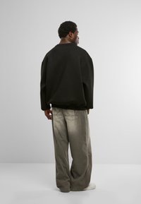 Mustmustrik black oversized sweatshirt lange õlgadega, seotud heledate hallide laiad püksid. Valged tossud ja õrnad õmblusdetailid on nähtavad.