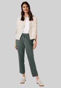 Light beige linen jacket over a white t-shirt paired with dark green tapered pants and beige sneakers. Simple design with elastic waist.