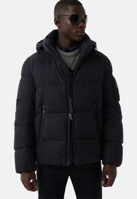 Granatowa pikowana kurtka z kapturem, wyposażona w zamki błyskawiczne z przodu i po bokach, pikowany wzór oraz prążkowany kołnierz dla dodatkowego ciepła.