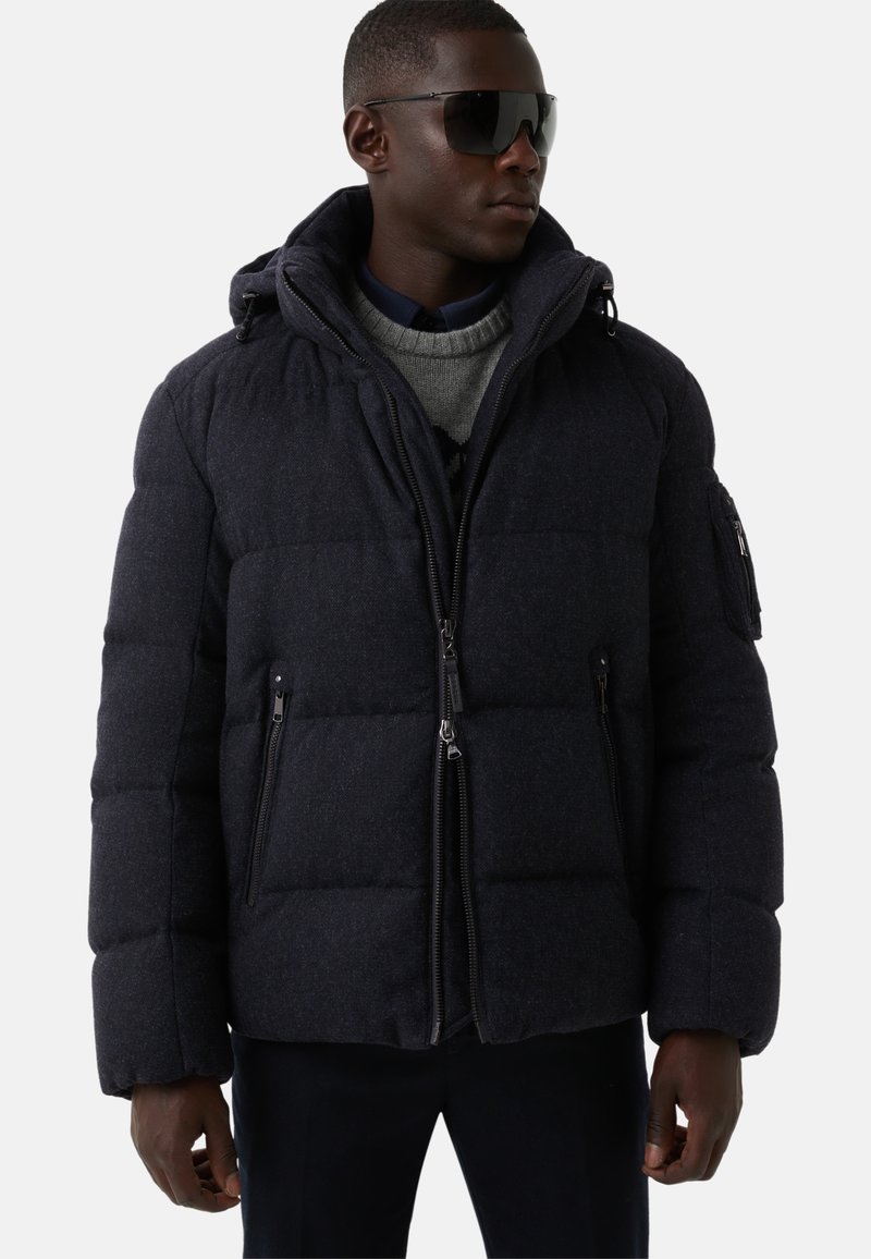 Granatowa pikowana kurtka z kapturem, wyposażona w zamki błyskawiczne z przodu i po bokach, pikowany wzór oraz prążkowany kołnierz dla dodatkowego ciepła.