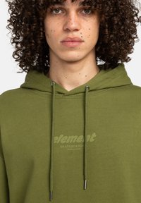 Olivengrøn hoodie lavet af blødt stof, med en front kangaroo lomme, snøre og et diskret logo trykt på brystet.