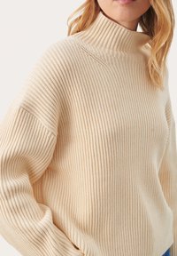 Beige ribbattu pusero, jossa on rento istuvuus, pystysuorilla tekstuureilla ja hieman ylikokoisilla hihoilla, valmistettu pehmeästä neulomateriaalista.