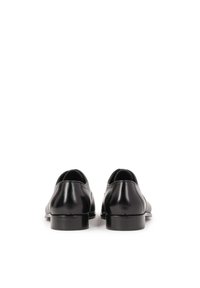 Scarpe in pelle nera con texture liscia, punta arrotondata e tacco basso, caratterizzate da un design minimalista e senza hardware visibile.