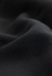 Mustast kangast lähivaade, millel on peen kudumistekstuur ja pehmed voldid, mis tekitavad õrnu varje ja helke.