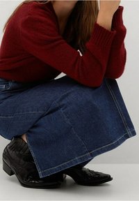 Burgundy neulepaita yhdistettynä sinisiin farkkuhameeseen. Mustissa cowboy-kengissä on teksturoitu muotoilu ja terävä kärki.