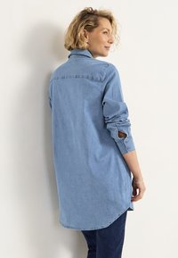 Helles blaues Denim-Hemd mit Kragen, langen Ärmeln und geknöpften Manschetten. Verfügt über einen abgerundeten Saum und einen lässigen Schnitt, der eine weiche Textur zeigt.