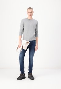 Grijze katoenen trui, blauwe denim jeans, donkere sneakers en een crèmekleurige tote tas. Het ensemble heeft een aansluitend ontwerp en geribde manchetten.